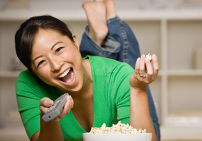 Happy woman laying on floor with bowl of popcorn, remote control